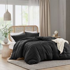 a bed with black comforter and pillows on top of it in a room next to a window