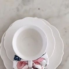 an empty cup and saucer sitting on top of a white plate with pink flowers