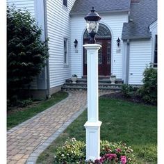 a white lamp post in front of a house with flowers around it and a walkway leading to the door