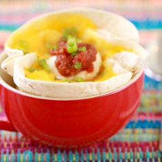 a red bowl filled with food sitting on top of a colorful table cloth next to a cup