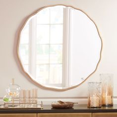 a round mirror sitting on top of a wooden dresser next to a vase and candles