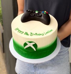 a person holding a birthday cake with a video game controller on it's top