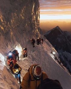 a group of people climbing up the side of a snow covered mountain at night time