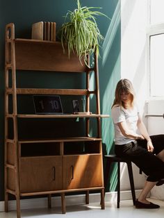 a woman sitting on a chair in front of a book shelf next to a potted plant