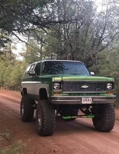 a green truck parked on the side of a dirt road