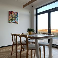 a dining room table with four chairs and a painting on the wall in front of it