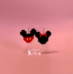 a pair of black and red mickey mouse earrings on clear acrylic stand against a pink background