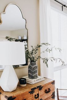 a white lamp sitting on top of a wooden dresser next to a mirror and plant