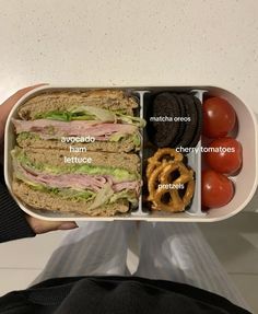 a person holding a tray with sandwiches and pretzels in it, along with other foods