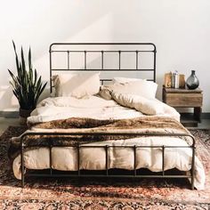 a bed sitting on top of a rug next to a wooden table with a potted plant