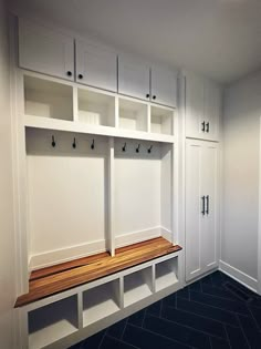 an empty room with white cabinets and wooden bench in the center, along with black tile flooring