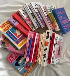 a pile of books sitting on top of a white bed covered in sheets and pillows