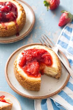 two plates with cheesecakes and strawberries on them, one has a bite taken out