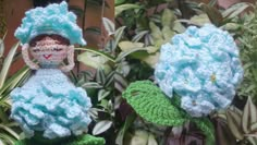 two crocheted dolls sitting next to each other in front of plants and flowers