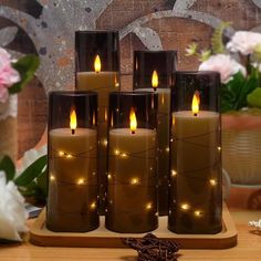 five lit candles sitting on top of a wooden table next to flowers and vases