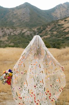 a woman in a dress with flowers covering her face and back from the sun, holding a bouquet of wildflowers