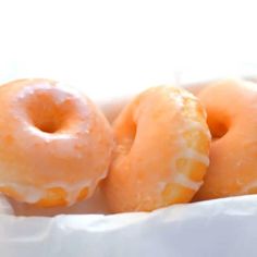 three glazed donuts in a white paper bag