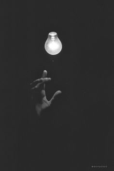 a hand is reaching up towards a light bulb in the dark with one hand out