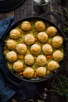 a pot filled with meatballs and vegetables on top of a wooden table next to wine glasses