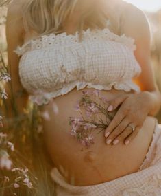 a pregnant woman with pink flowers on her stomach in the middle of some wildflowers