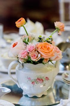 a white tea pot with pink and orange flowers in it sitting on a silver tray