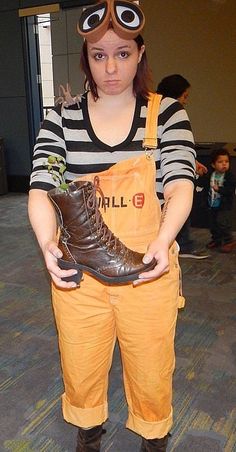 a woman in an orange overalls holding a pair of boots with googly eyes