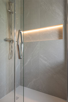 a bathroom with a glass shower door and white tile walls, along with a light strip on the wall