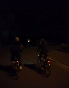 two people riding bikes at night in the dark