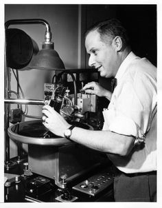 black and white photograph of a man working on an old fashioned machine with a lamp in the background