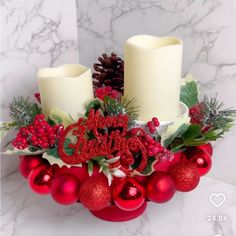 two candles are sitting on top of a wreath with red balls and greenery around it