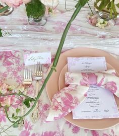 the table is set with pink flowers and place settings