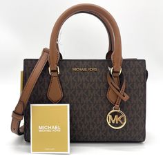 Brand New With Tag Michael Kors Sheila Small Satchel Shoulder Crossbody Bag Vegan Leather Gold Toned Hardware Color: Brown 100% Authentic **Please See The Measurement For The Size** No Dust Bag Michael Kors Logo At Front 1 Mk Charm Zip Top Closure Triple Compartment With Center Zip Custom Fabric Lining 1 Slip-In Pocket 9" (Bottom) X 6.5"(H) X 3"(D) Straps: 3.5" Adjustable Strap: 20.25"-23.75" Chic Brown Bag With Logo, Coated Canvas Satchel With Logo, Brown Satchel Bag With Logo, Brown Logo Satchel For Travel, Rectangular Brown Satchel With Logo, Brown Rectangular Satchel With Logo, Michael Kors Top Handle Shoulder Bag With Logo, Brown Top Handle Satchel With Logo, Logo Crossbody Satchel For Travel