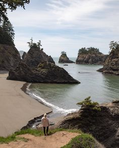 a man standing on top of a sandy beach next to the ocean with rocks in the background