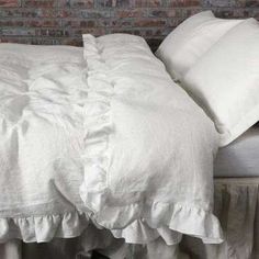 there is a bed with white linens and pillows on top of it, next to a brick wall