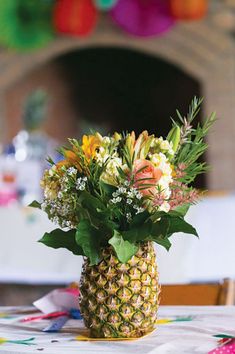 a pineapple vase filled with colorful flowers on top of a white tablecloth covered table