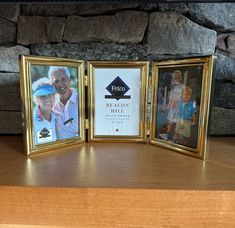 three gold frames with photos of people in them on a wooden table next to a stone wall