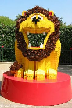 a large lego lion sitting on top of a red stand in front of a hedge