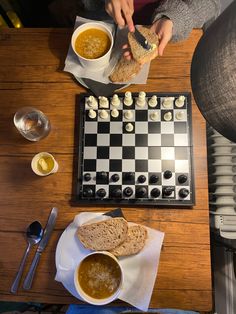 a person sitting at a chess board with soup and bread in front of them on the table