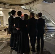 four people standing in front of a staircase with their arms around each other and looking at something on the ground