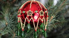 a red ornament hanging from a pine tree with beads and beadwork