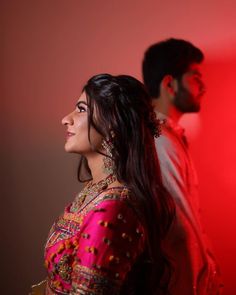 a man and woman standing next to each other in front of a red wall,