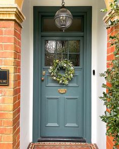 a blue front door with a wreath hanging on it's side and brick pillars