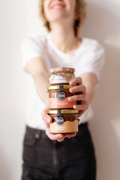 a woman holding three jars of food in her hands