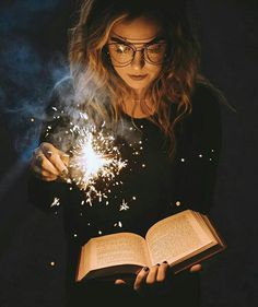 a woman reading a book while holding a sparkler in her hand and looking at it