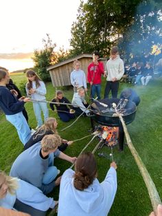 a group of people standing around a bbq on top of a grass covered field