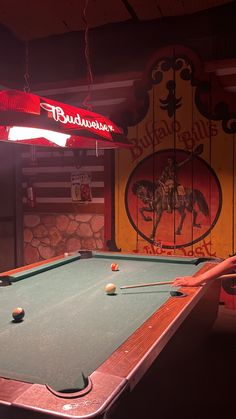 a pool table in a room with a neon sign on the wall and other items around it