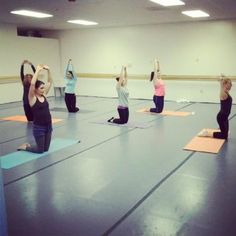 a group of people doing yoga in a room with their arms up and legs crossed