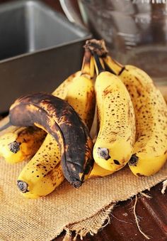 three ripe bananas sitting on top of a table next to a metal bowl and pan