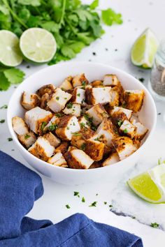 a white bowl filled with tofu and garnished with cilantro next to limes