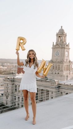 a woman in white dress holding up gold letter balloons